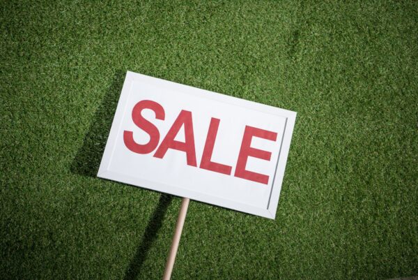 white sale banner lying on green grass, house for sale concept
